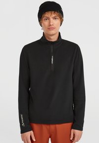 Sort halv-zip fleece-top med lange ærmer, der har et Polartec-logo på manchetterne og et O'Neill-logo på lynlåsen. Glat tekstur.