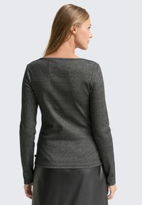 Czarna bluzka z długim rękawem o subtelnej metalicznej poświacie, z wykrojem w serek na plecach i gładkiego materiału. Podkreślona dopasowaną sylwetką.