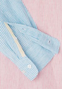 Helles blau gestreiftes Hemd mit weißen Knöpfen, das über einen kontrastierenden gelben Besatz an der Knopfleiste und einen strukturierten rosa-weißen Streifenhintergrund verfügt.
