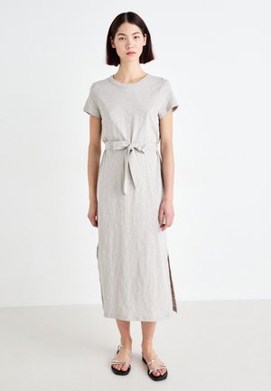 Robe grise clair à mi-longueur avec des manches courtes, une taille à nouer, des fentes sur les côtés et un tissu doux. Associée à des sandales noires à lanières.