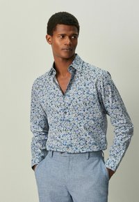 Camisa de manga larga con estampado floral en azul claro, con flores blancas y azules oscuras. Con botones en la parte delantera y cuello abierto. Tejido de algodón suave.