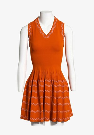 Robe orange sans manches avec col en V et détails de coutures ondulées blanches le long du décolleté et des plis de la jupe, présentée sur un mannequin blanc.