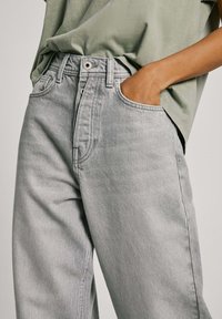 Ljusgrå denimjeans med rak skärning, framfickor och knäppning. Kombinerat med en löst sittande grön T-shirt.