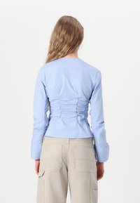 Camicia azzurro chiaro a maniche lunghe con dettagli arricciati sul retro, caratterizzata da un colletto tondo e una silhouette aderente; abbinata a pantaloni cargo beige.