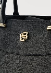 Μαύρη δερμάτινη τσάντα με υφή, με διπλό χρυσό λογότυπο "B" και αντιστοιχίες σε χρυσές λεπτομέρειες στη λαβή.