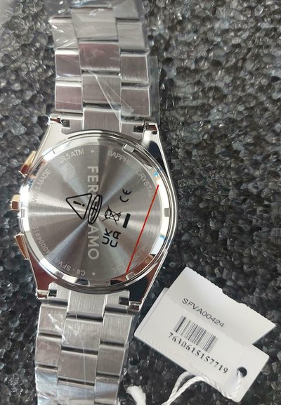 Reloj de acero inoxidable plateado con esfera redonda, cristal de zafiro y pulsera de eslabones. Las características incluyen un logo e indicadores de resistencia al agua.