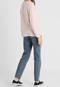 Rosa långärmad topp med rund halsringning, parat med blå denimjeans med fransiga fållar och svarta canvas sneakers.