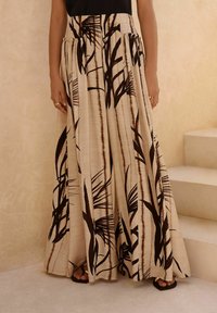 Jupe longue beige en tissu texturé, avec des motifs de feuilles de palmier brun foncé et une taille froncée avec des poches latérales.