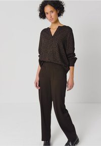 Czarna bluzka w panterkę z dekoltem w serek i długimi rękawami, zestawiona z ciemno brązowymi spodniami o wysokim stanie. Gładka tkanina i luźny krój.