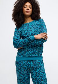 Mikina s potlačou leopardieho vzoru v tyrkysovej farbe, s dlhými rukávmi a rebrovanými manžetami, v kombinácii so zodpovedajúcimi nohavicami s leopardím vzorom, oboje z mäkkej látky.