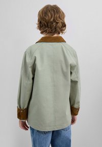 Jachetă oversized verde cu guler din catifea maro, manșete cu nasturi și o textură netedă. Vederea din spate prezintă un design simplu și detalii de cusătură.