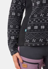 Polarowa bluzka w czarnym kolorze z białymi geometricznymi wzorami i płatkami śniegu. Panel boczny z akcentem w postaci szwedzkiej flagi.