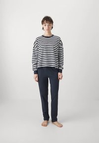 Haut à manches longues rayé noir et blanc avec un col rond, associé à un pantalon bleu marine. Tissu en mélangé de coton, coupe décontractée.