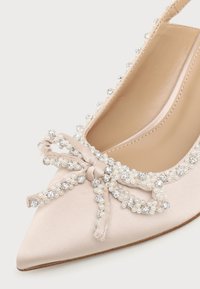 Chaussure plate en satin beige à bout pointu décorée d'un nœud et ornée de petites perles et strass.