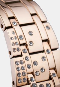 Zapestnica za uro v rožnato zlato z geometričnim dizajnom, vključno z vgrajenimi rhinestones, gladkimi kovinskimi segmenti in sijajno površino.