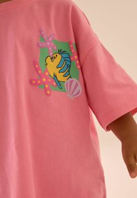 Lyserød bomulds t-shirt med et farverigt grafisk motiv af en fisk og koralfarver. Løs pasform med korte ærmer og rund halsudskæring.