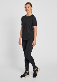 Sort atletisk T-shirt med korte ærmer og rund hals, parret med sorte leggings og sorte sneakers med et struktureret design.
