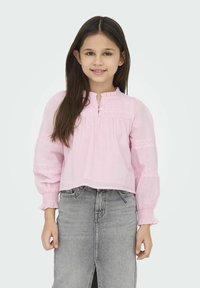 Rosa långärmad blus med volangkrage, knapprad och broderade detaljer på ärmarna, i kombination med en grå denimkjol.