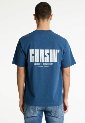 Blaues Baumwoll-T-Shirt mit großem weißen Text "CHASIN'" und kleinerem Text darunter. Klassischer Rundhalsausschnitt und kurze Ärmel, entspannter Schnitt.