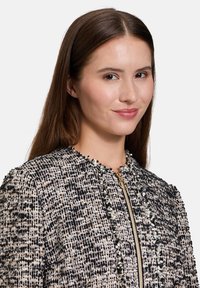 Textúrás tweed dzseki fekete és bézs mintával, arany cipzárral és rojtos részletekkel a galléron és az éleken.