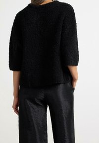 Musta tekstuuriga lühikeste varrukatega sviiter, lahtine lõige ja pehme, koheva materjaliga, kombineeritud läikivate mustade pükstega, millel on peene kortsukujundus.