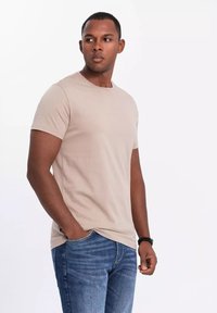 Beżowa bawełniana koszulka z krótkim rękawem i okrągłym dekoltem, w połączeniu z niebieskimi dżinsami. Gładka tekstura, dopasowany krój i casualowy styl.