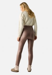 Leggings marrones de cintura alta con un acabado suave, combinados con un suéter crema y unos zapatos beiges con puños de punto y hebilla.