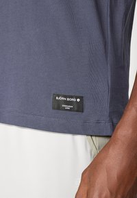 Marineblå t-skjorte laget av bomull med synlige sømmer, med en sydd svart etikett som viser "BJÖRN BORG" og "STOCKHOLM 1956."