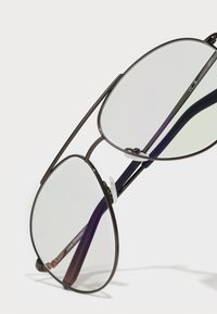 Óculos de sol estilo aviador com grandes lentes cinza translúcidas, uma armação metálica preta e fina, e hastes com tom púrpura apresentando almofadas de nariz transparentes.