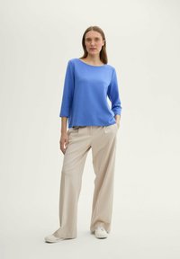 Blaues Langarmshirt mit rundem Halsausschnitt, kombiniert mit beigen weit geschnittenen Hosen und weißen Sneakers. Schlichtes Design und glatte Textur.