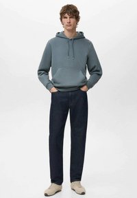 Jasnoniebieska bluza z kapturem z przednią kieszenią i troczkami, połączona z ciemnymi dżinsami i beżowymi sneakersami. Prosty, casualowy styl.