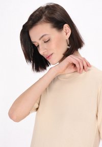 Beige pletený top s krátkým rukávem a vysokým výstřihem, se žebrovanou texturou a jemnými detaily švů. Jednoduchý design bez vzorů.