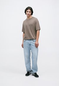 Brown short-sleeve t-shirt paired with light blue baggy jeans and black shoes. The fabric appears soft with a relaxed fit.