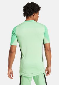 Maglietta sportiva a maniche corte in verde menta, con accenti neri sui lati e una texture liscia e traspirante. Logo visibile sulla parte bassa della schiena.