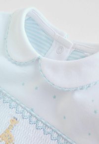 Indumento bianco per neonato con collo a camicia, ricamo blu, motivi a stelle e pannello testurizzato con disegno di giraffa.
