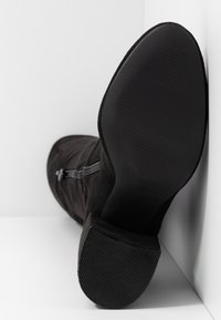 Bottine noire en daim avec une semelle en caoutchouc texturée, une fermeture éclair latérale et une finition lisse. Design profilé avec un talon légèrement courbé.