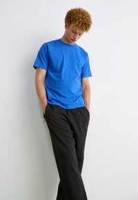 Camiseta de algodón azul con cuello redondo y mangas cortas, combinada con pantalones de chándal negros. La tela parece suave y ligeramente texturizada.