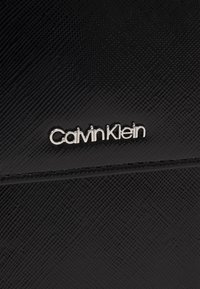 Czarny portfel o teksturowanej powierzchni z subtelnym wzorem, z widocznie umieszczonym srebrnym logo "Calvin Klein" na przedniej stronie.