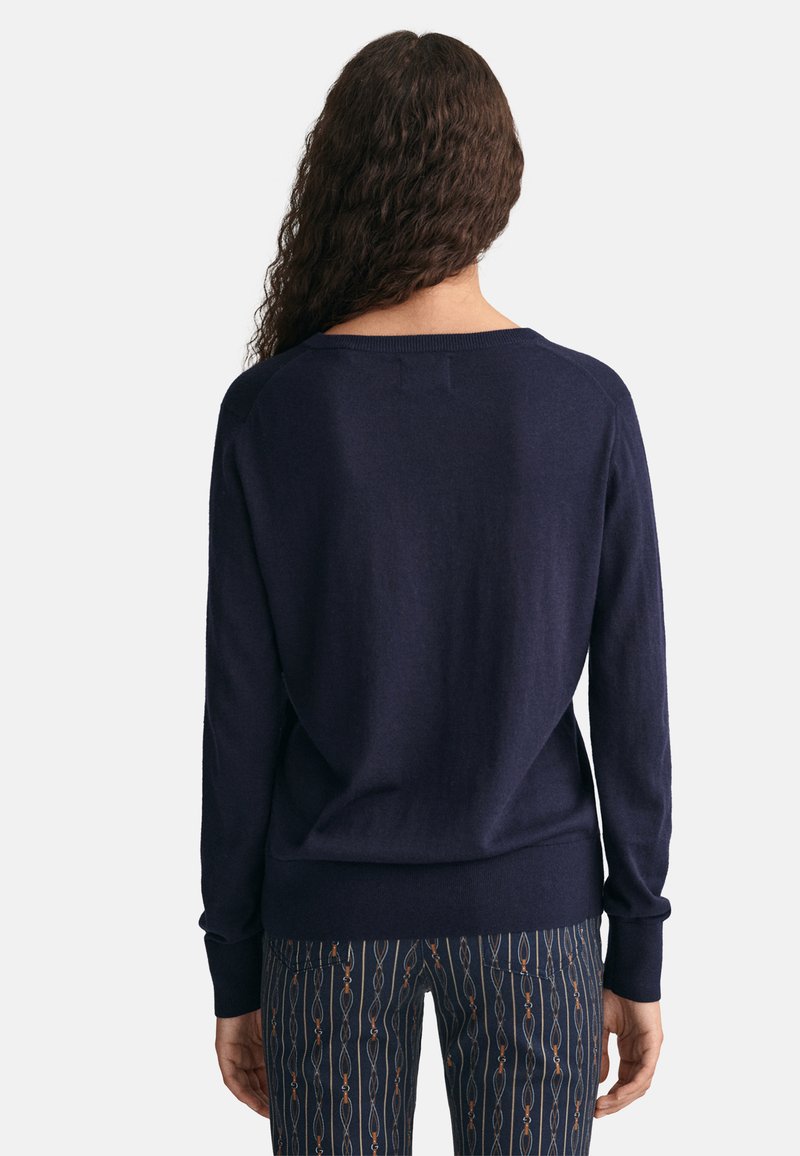 Marineblaues Strickpullover mit lockerer Passform, weitem Ausschnitt und langen Ärmeln, kombiniert mit gemusterten Hosen, die verlängerte Formen zeigen.