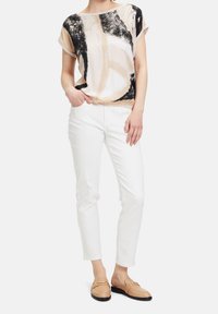 Koszulka z krótkim rękawem w abstrakcyjny wzór w kolorze beżowym, czarnym i kremowym. W zestawie z wąskimi białymi spodniami i jasnobrązowymi mokasynami. Gładka tekstura materiału.