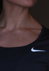 Top sportivo nero con scollatura rotonda, realizzato in tessuto testurizzato. Presenta un prominente logo bianco Nike sul lato sinistro.