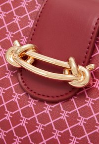 Bordowa skórzana torba z błyszczącym złotym łańcuchem i zapięciem, z różowym geometrycznym wzorem na powierzchni oraz precyzyjnym przeszyciem.