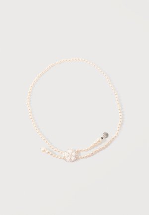 Collier de perles à double rang avec un fermoir en argent en forme de fleur et une petite étiquette ronde en argent sur un fond clair.
