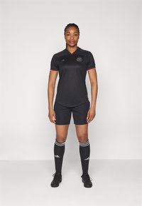 Svart fotbollskit med korta ärmar, med röda detaljer på kragen och ärmarna, svarta shorts och knälånga svarta strumpor med vita ränder.