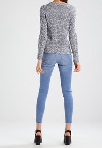 Harmaa ja valkoinen, teksturoitu, pitkähihainen neulepaita yhdistettynä vaaleansinisiin kapealahkeisiin farkkuihin ja mustiin korkokenkiin. Asukokonaisuuden takanäkymä.