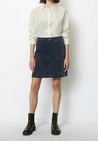 Mini gonna in velluto a coste blu scuro con chiusura frontale a bottoni, abbinata a una camicia panna con bottoni e stivaletti neri.