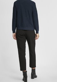 Granatowy sweter o fakturze z wypukłymi kropkami, zestawiony z czarnymi, zwężanymi spodniami. Czarne botki na słupku. Prosty design, minimalistyczny wygląd.