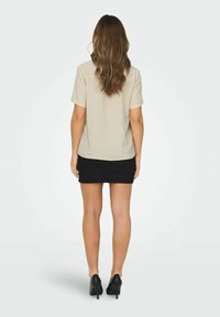 Beige T-shirt met korte mouwen in een relaxte fit, gecombineerd met een strakke zwarte mini-jurk, gedragen met zwarte hoge hakken.