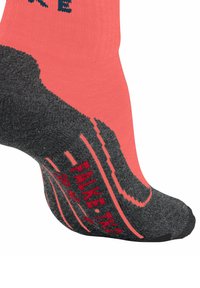Koralowa i ciemnoszara skarpetka z teksturowaną powierzchnią, z wzorem antypoślizgowym na podeszwie oraz napisem „FALKE” w czerwonych literach.
