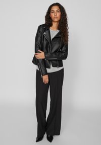 Black faux leather biker jacket with silver zippers, layered over a gray t-shirt, paired with loose black trousers and pointed black shoes.